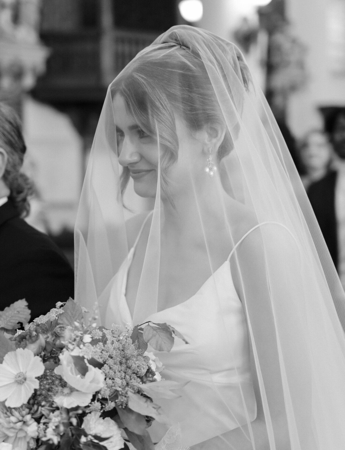 A bride smiles at her groom from under her cathedral veil, walking down the aisle of St. Peter and Paul church