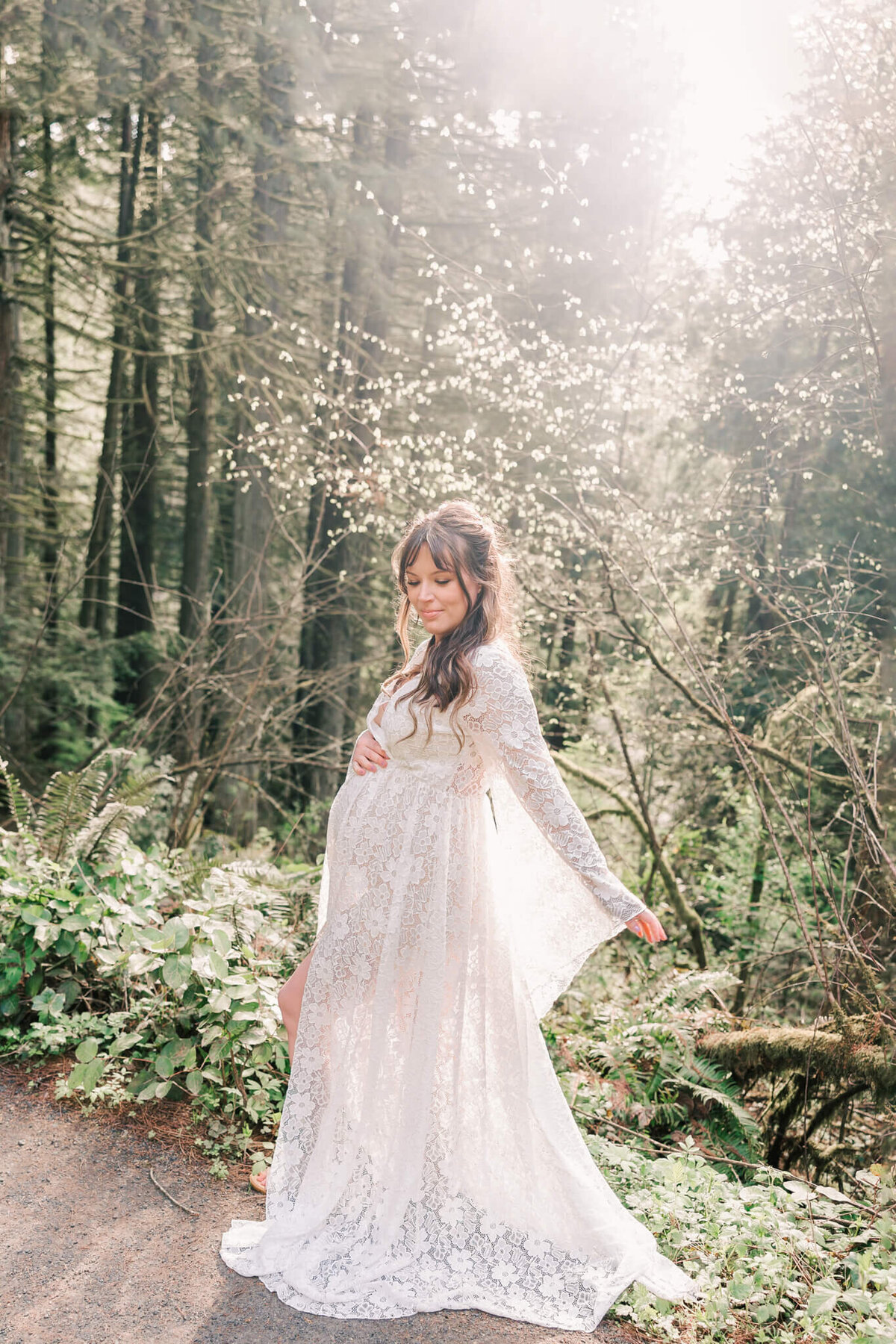 Portrait on a woman walking through the forest in portland, oregon. She has her white lace dress flowing behind her and the sun shining over top of her through the green trees.