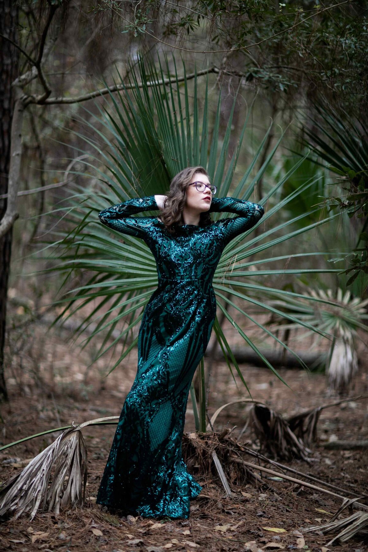 senior in green sequin dress posed in front of tree