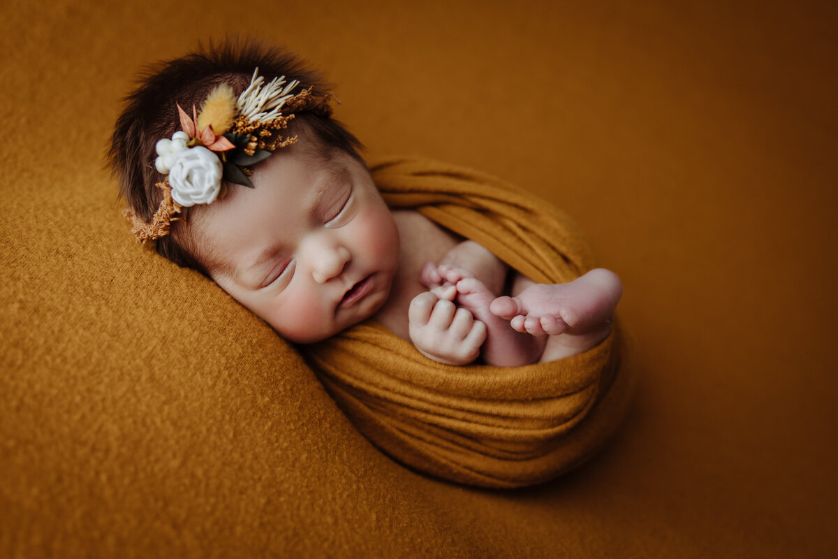 baby girl in a loose golden color wrap with hands and toes showing