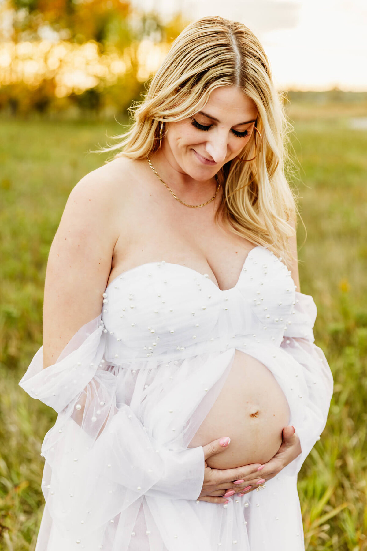 beautiful mom holding her baby bump and smiling captured by Ashley Kalbus Photography
