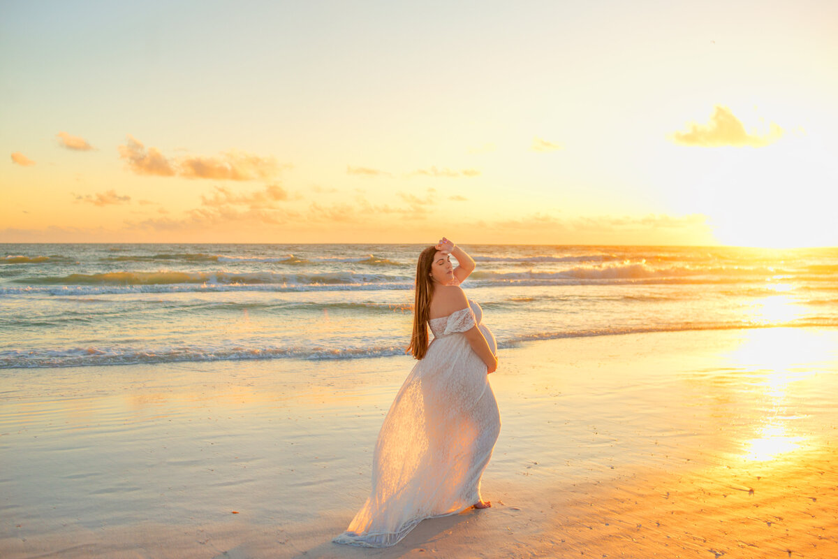 Women standing on the beach wearing white gown  during maternity photoshoot with Franklin Tennessee maternity photographer