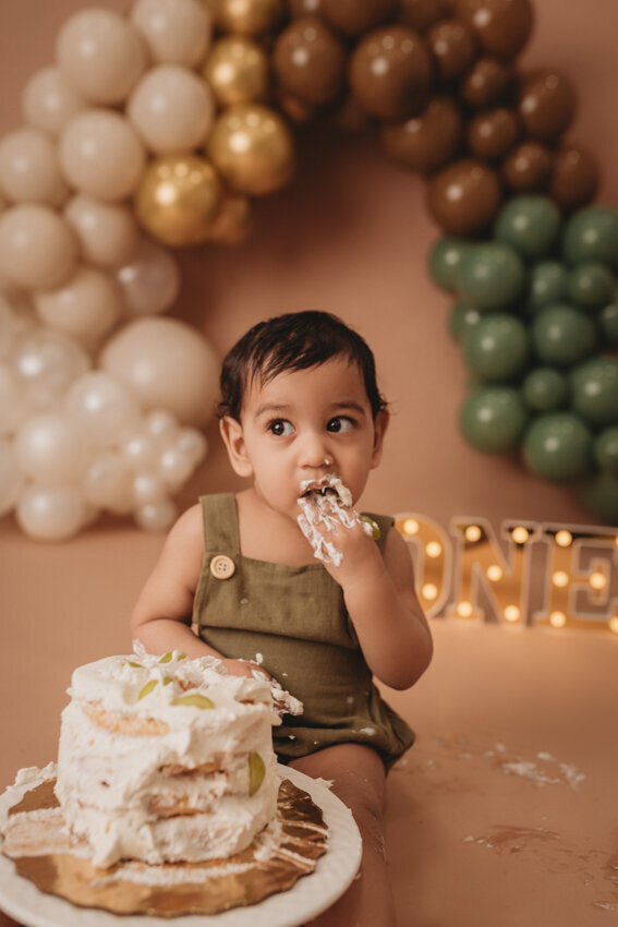 Cake smash milestone session with Atlanta, Georgia cake smash photographer. Milestone photography session with earthy tones, balloon garland and sweet baby boy eating cake for his first birthday.
