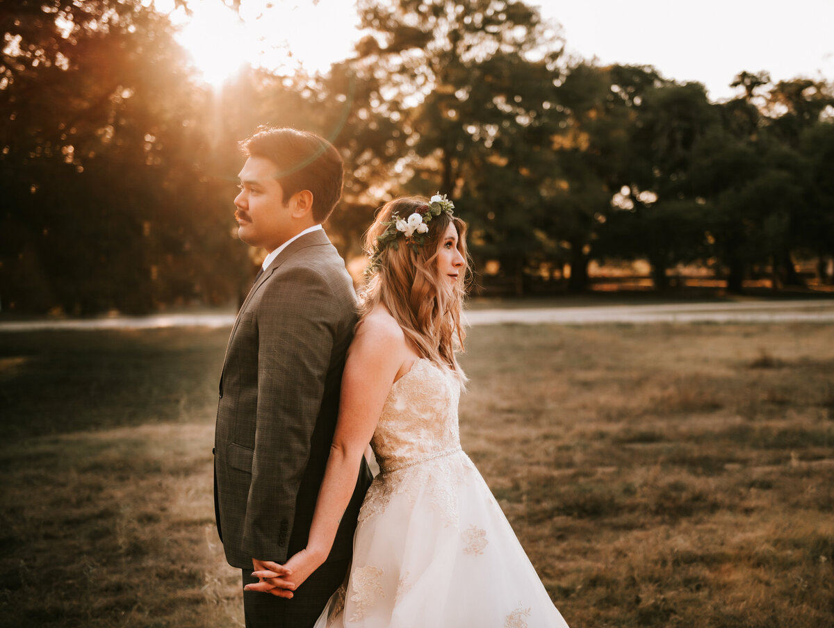 Couples Photography, A bride and groom stand back to back holding hands in a park