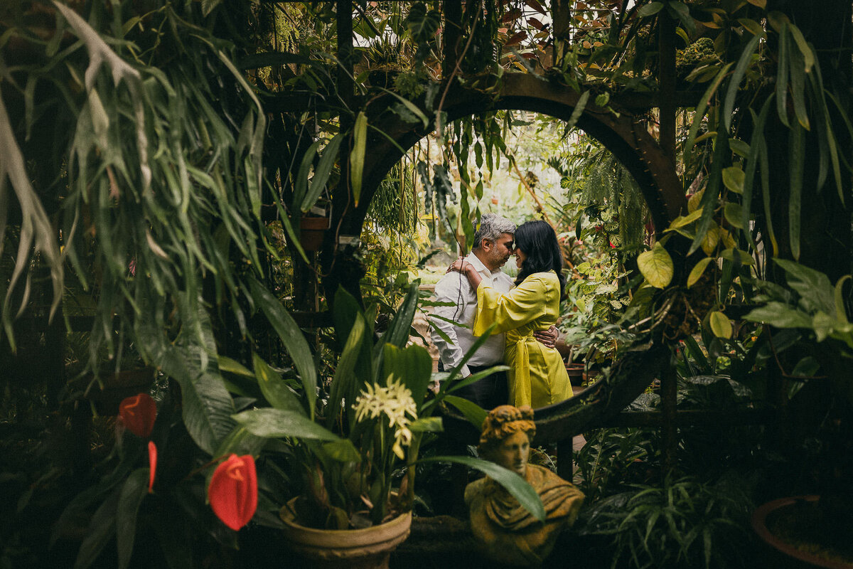 Bay Area elopment photography session at San Francisco Conservatory of Flowers.  Bridge wears yellow dress and red flowers are in front. Framed in circle with green foliage.