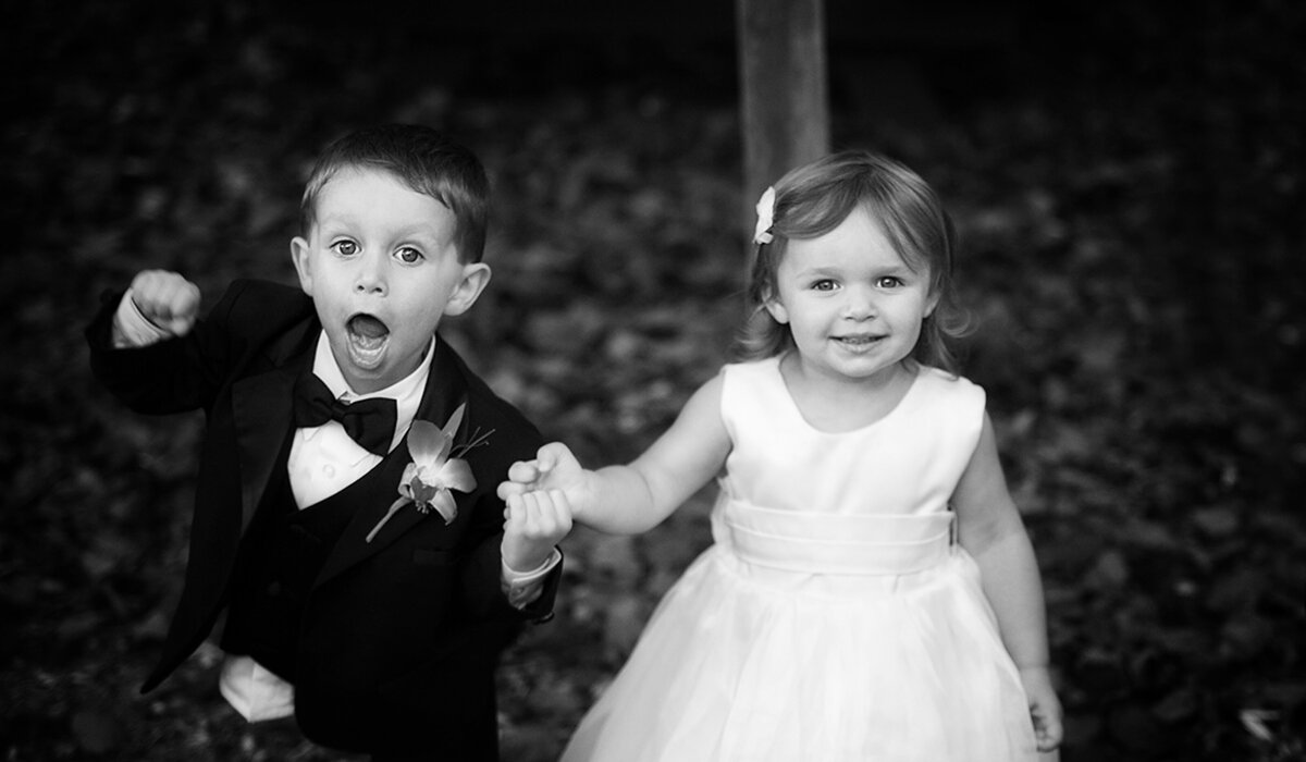 A cute ring bearer and flower girl hold hands at a wedding ceremony.
