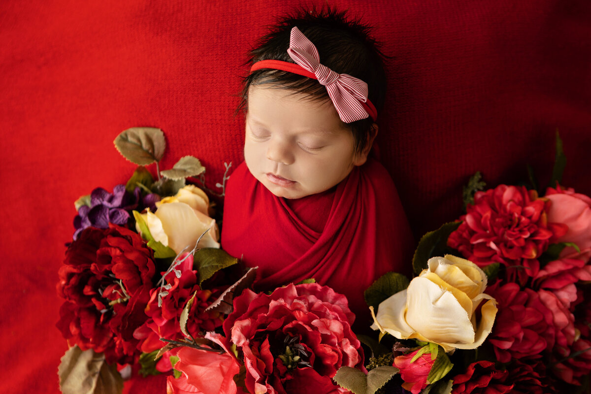 newborn in red wrap, red background and flowers