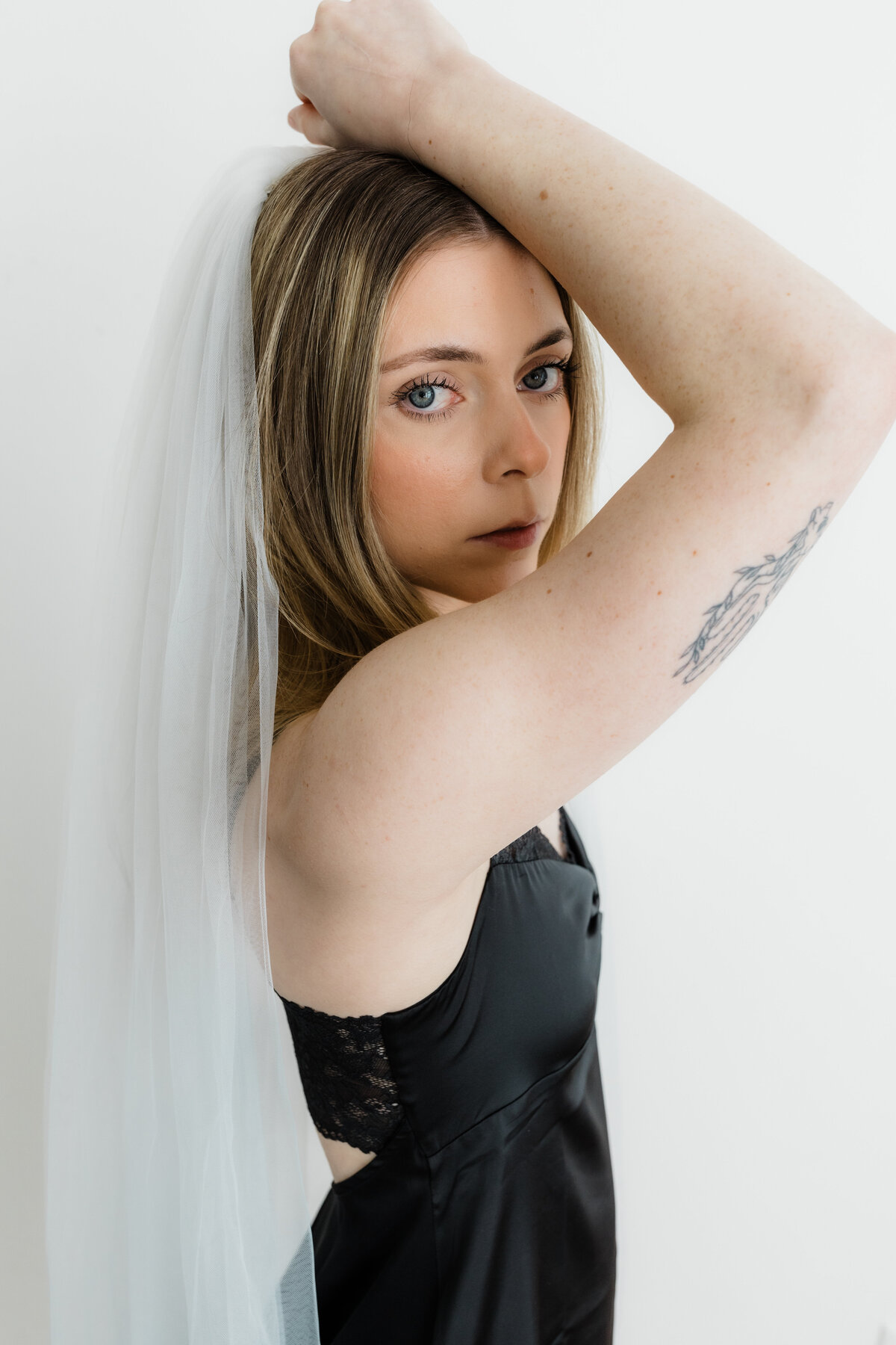 Woman confidently posing in black lingerie and a veil, captured during a bridal boudoir session.