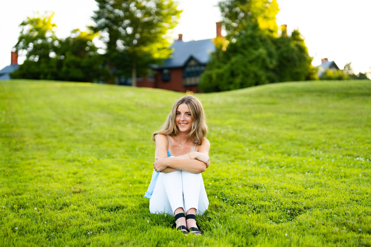 High school senior girl sitting on stone steps in a garden, surrounded by greenery.