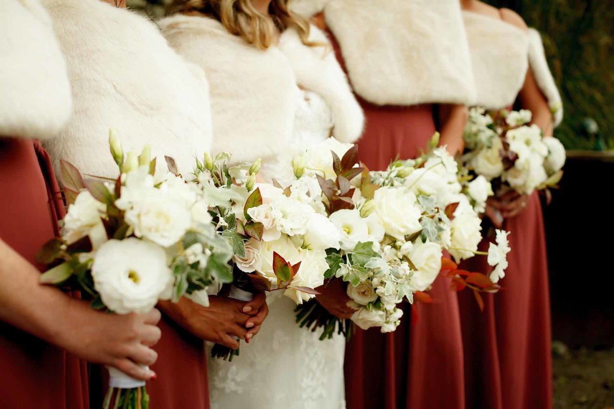 bride's maids holding fall flower bouquets of white roses, white dahlias, white scabiosa, with rust colored foliage