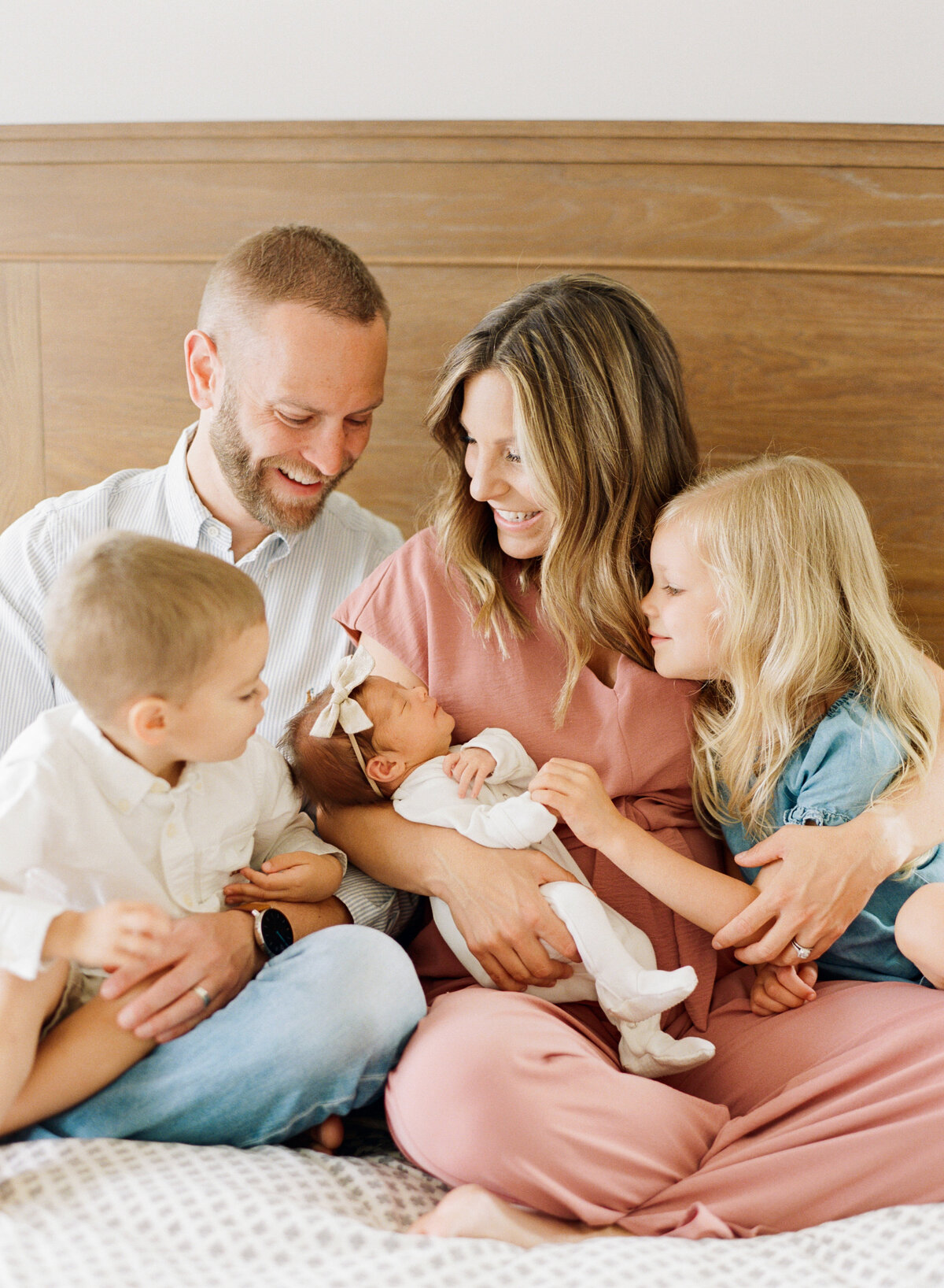 Family cuddles their new baby close while sitting on a bed. Image by Raleigh newborn photographer A.J. Dunlap Photography.