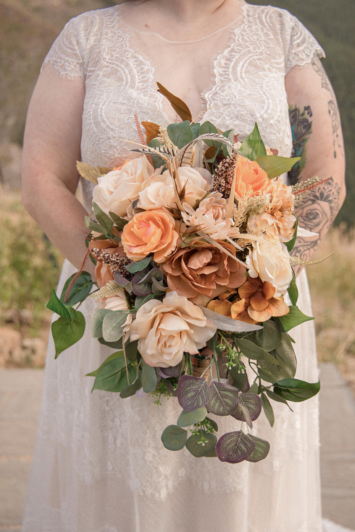 A close up photograph of the brides bouquet, showcasing orange, white and rust roses and a variety of green foliage