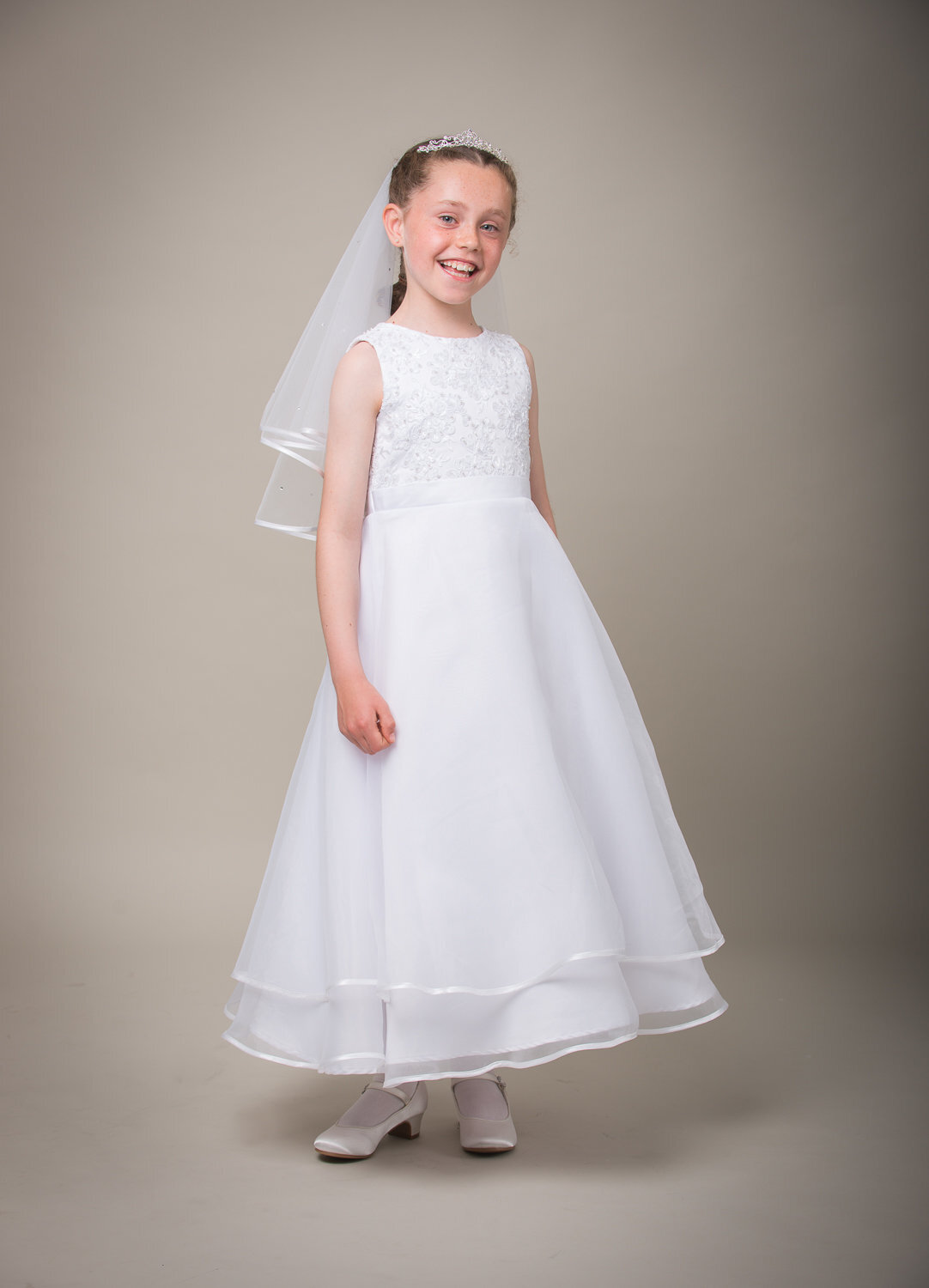 studio portrait of a girl smiling wearing white communion dress