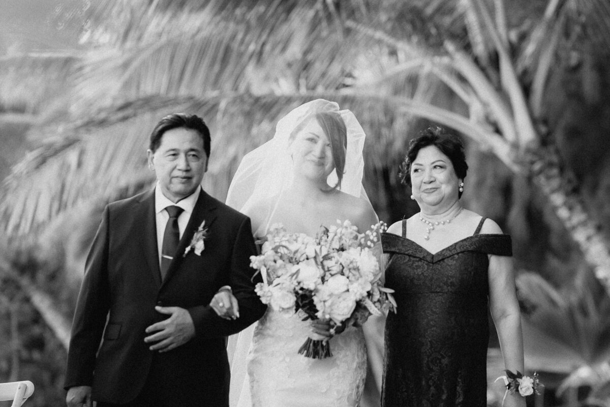 Bride walking with parents down the ceremony aisle in black and white