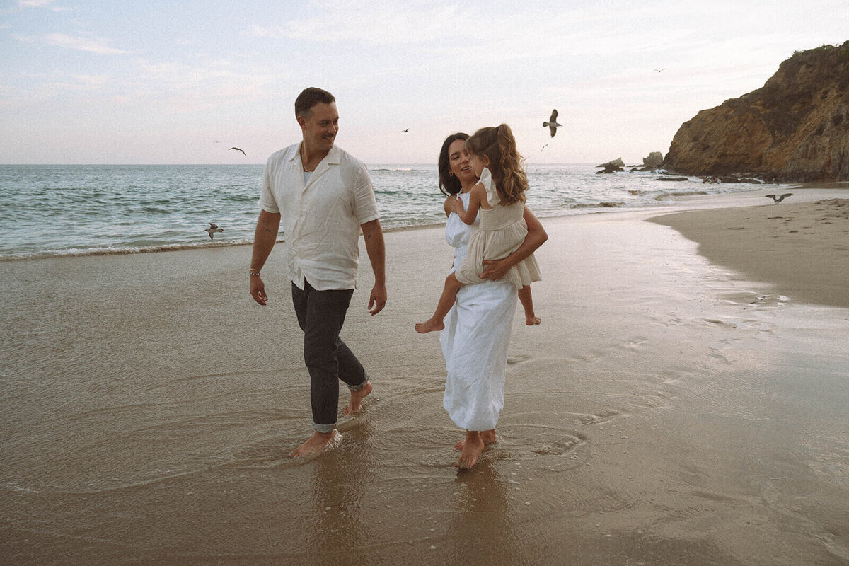 Family walking barefoot along the shoreline during a candid Laguna Beach family photography session at sunset in Orange County, California.