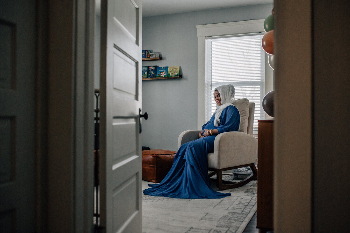 Maternity photoshoot with a woman sitting in a chair in a child's room.