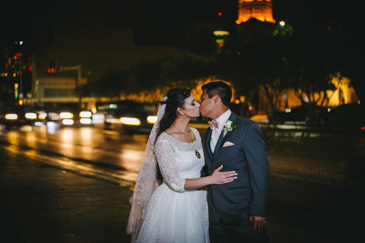 Bride kissing groom on a street corner in downtown San Antonio with the Tower of Life behind them.