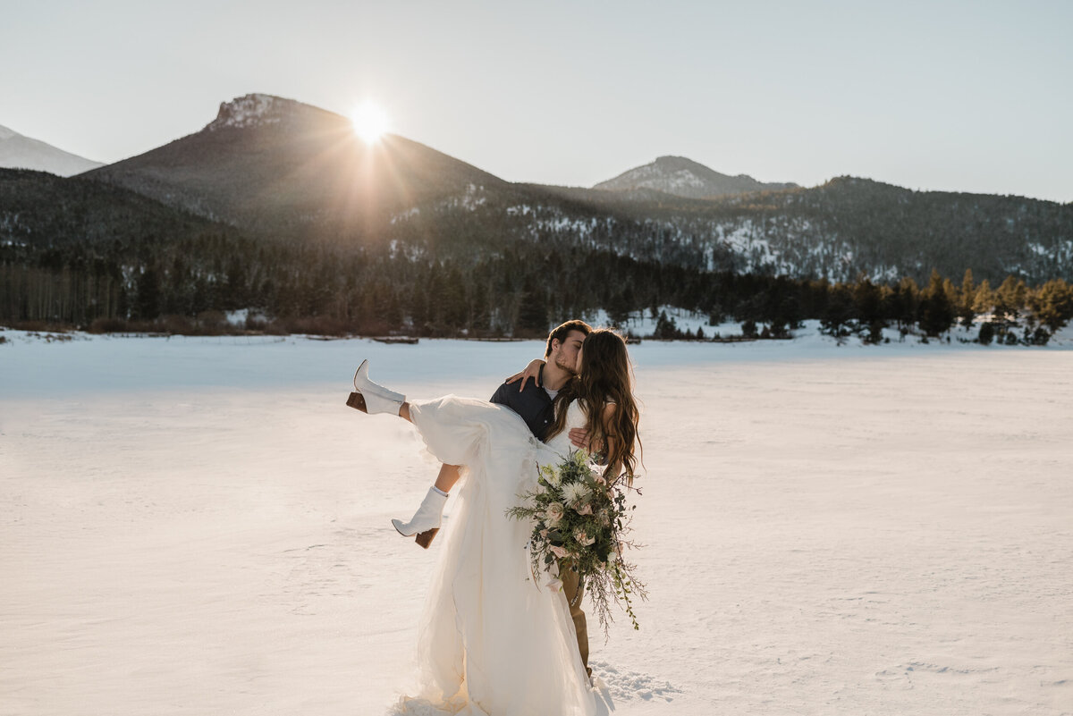 Couple shares a kiss on a frozen lake in the mountains during their elopement