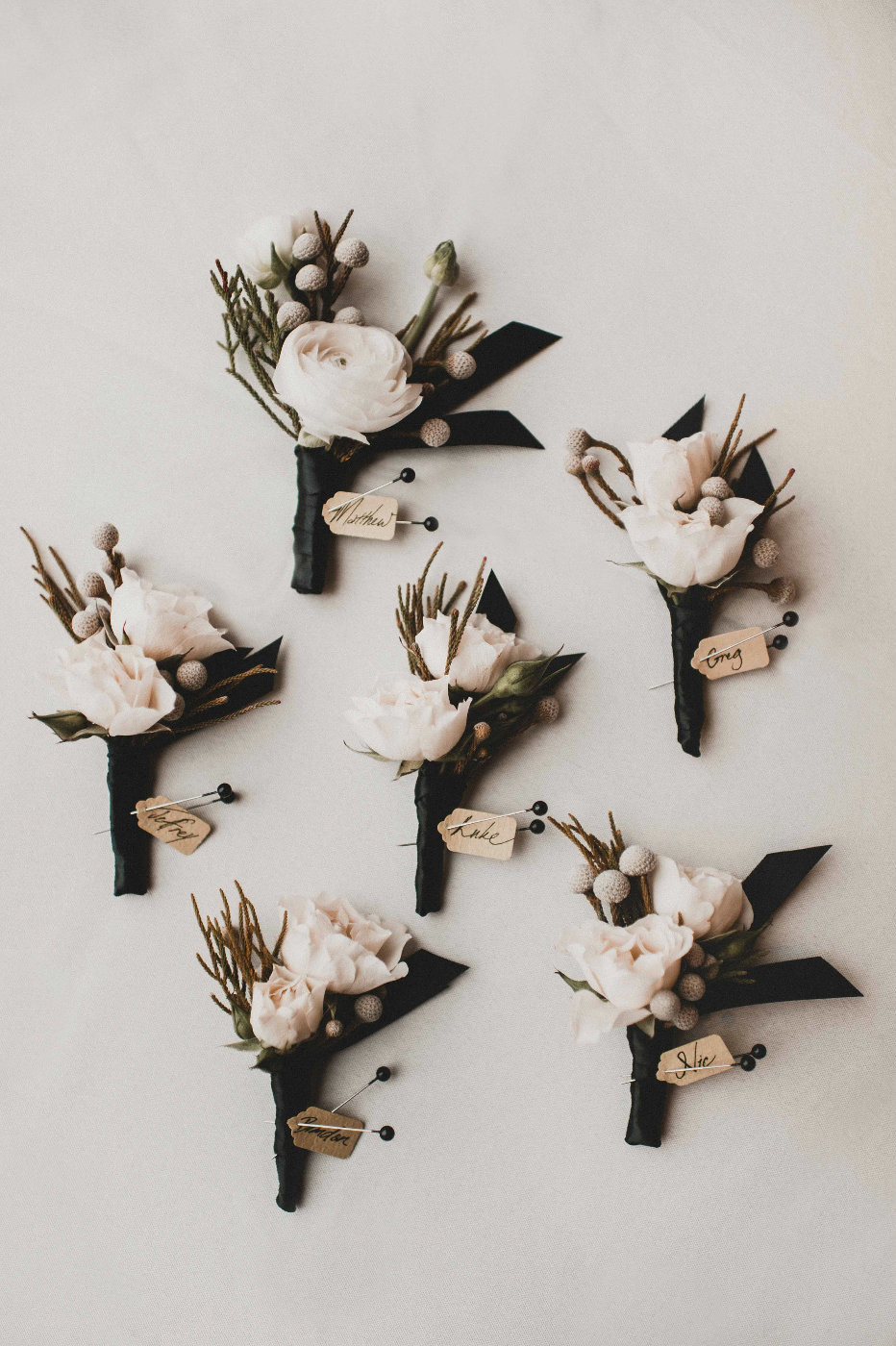 Wedding party boutonnieres white spray roses and silver brunia wrapped in black ribbon.