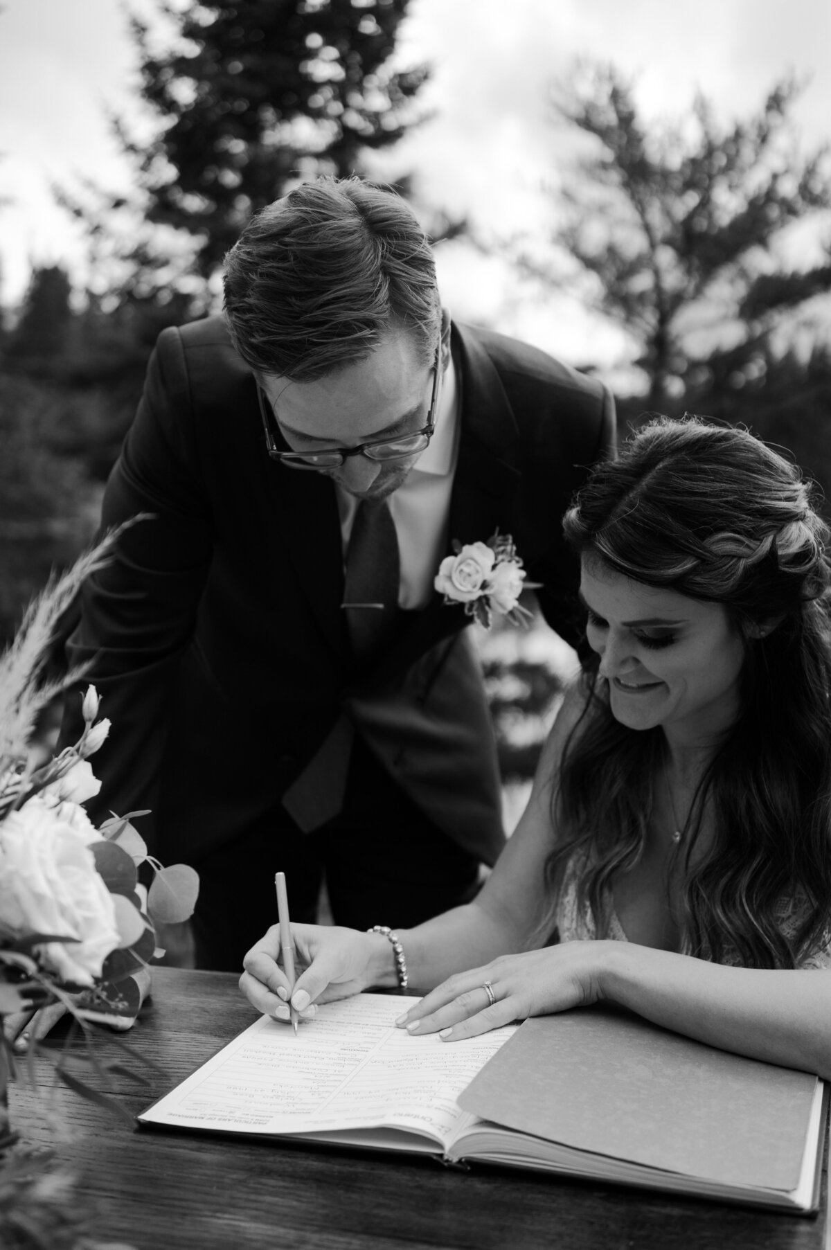 black and white image bride and groom signing paper