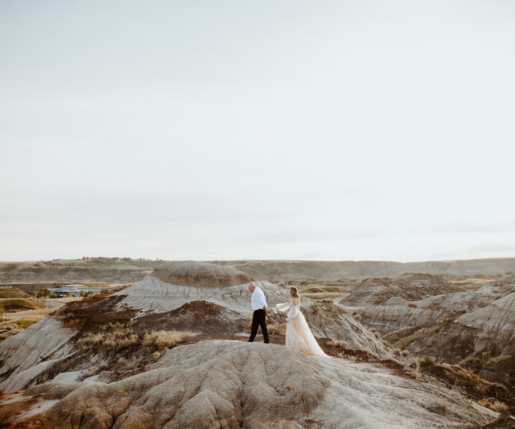 Couple holding hands on a stone hill, woman wearing elegant blush gown captured by Ninth Avenue Studios, authentic and intimate wedding photographer in Calgary, Saskatoon, and Vancouver. Featured on the Bronte Bride Vendor Guide.