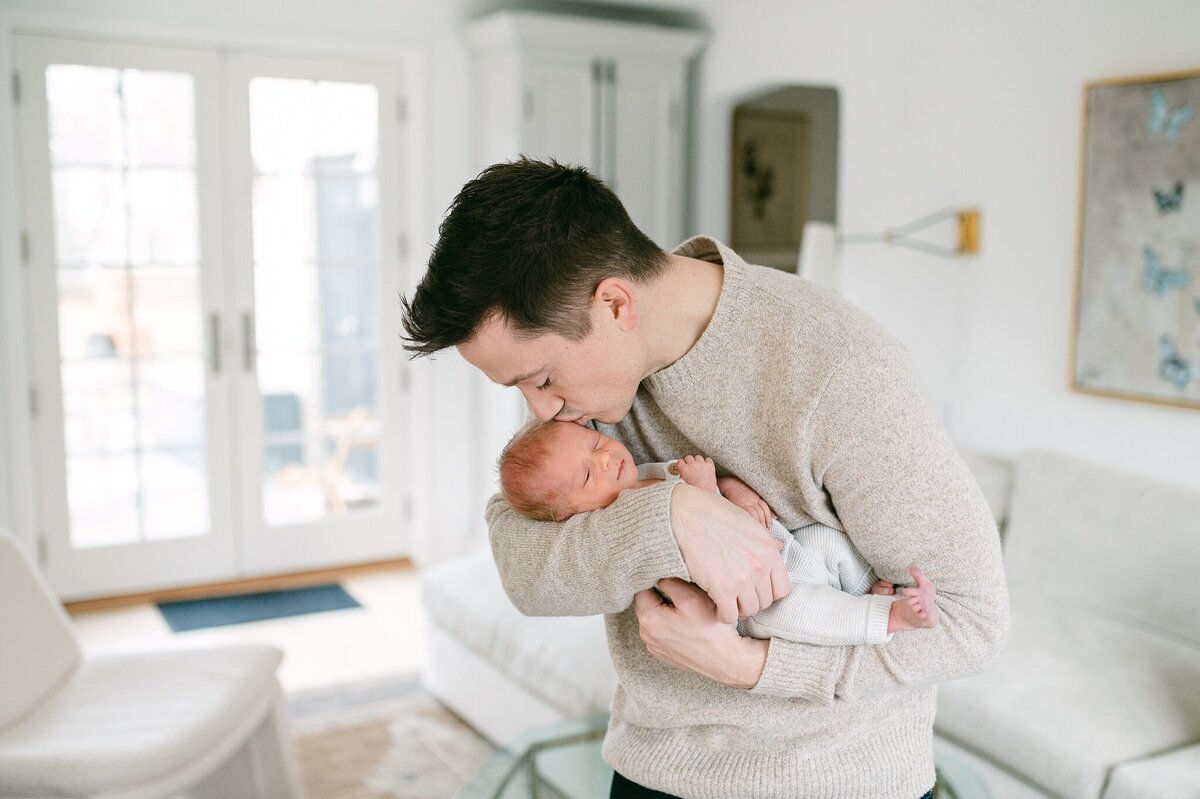 Dad leans over to kiss his newborn son on the cheek