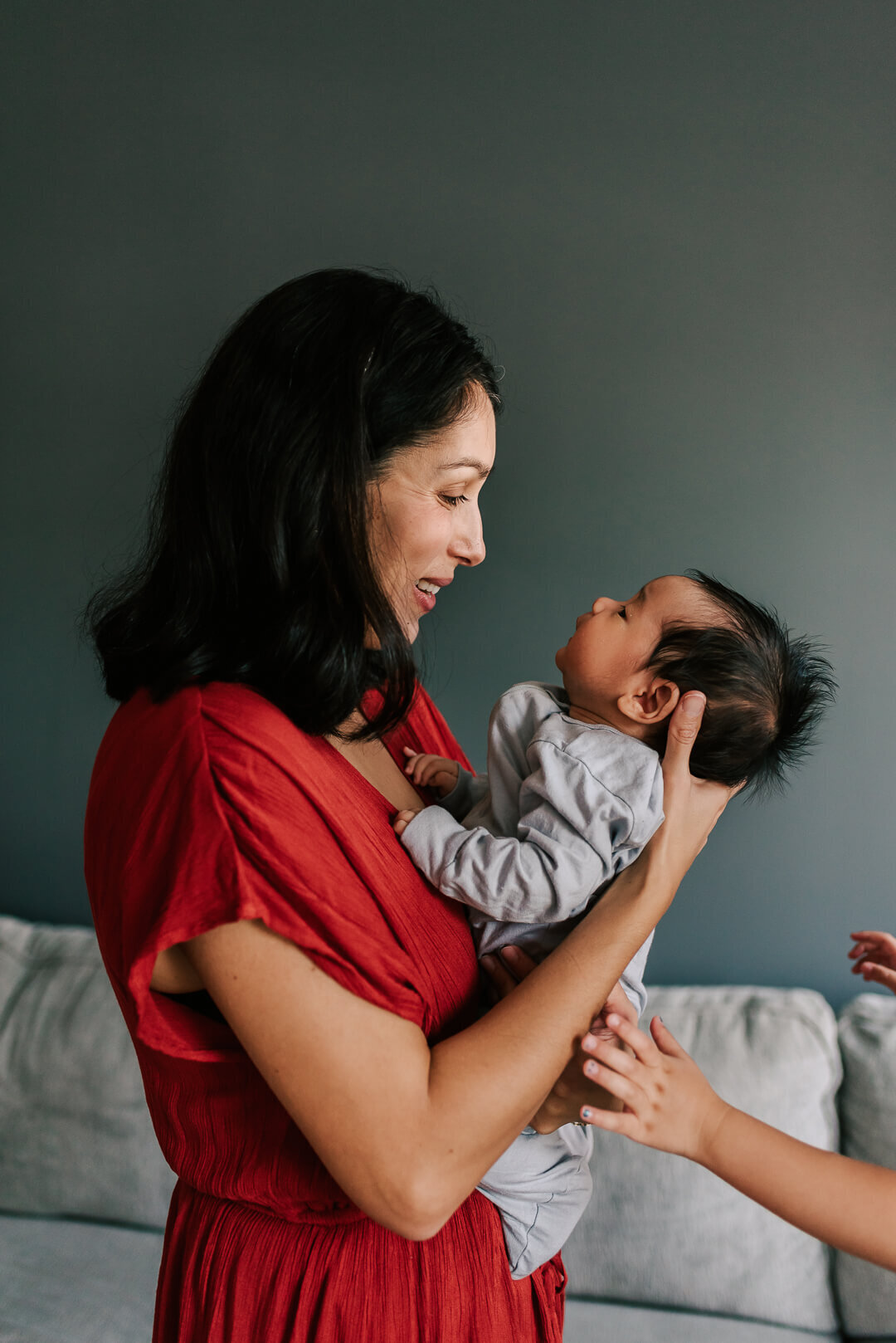 A mother beaming at her newborn son while her daughter's arms reach into the frame