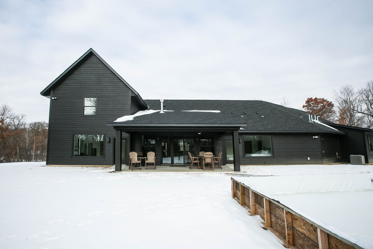 Exterior back view of custom home in Elk River, Minnesota with black siding, wood details and patio built by Cornerstone Custom Builds