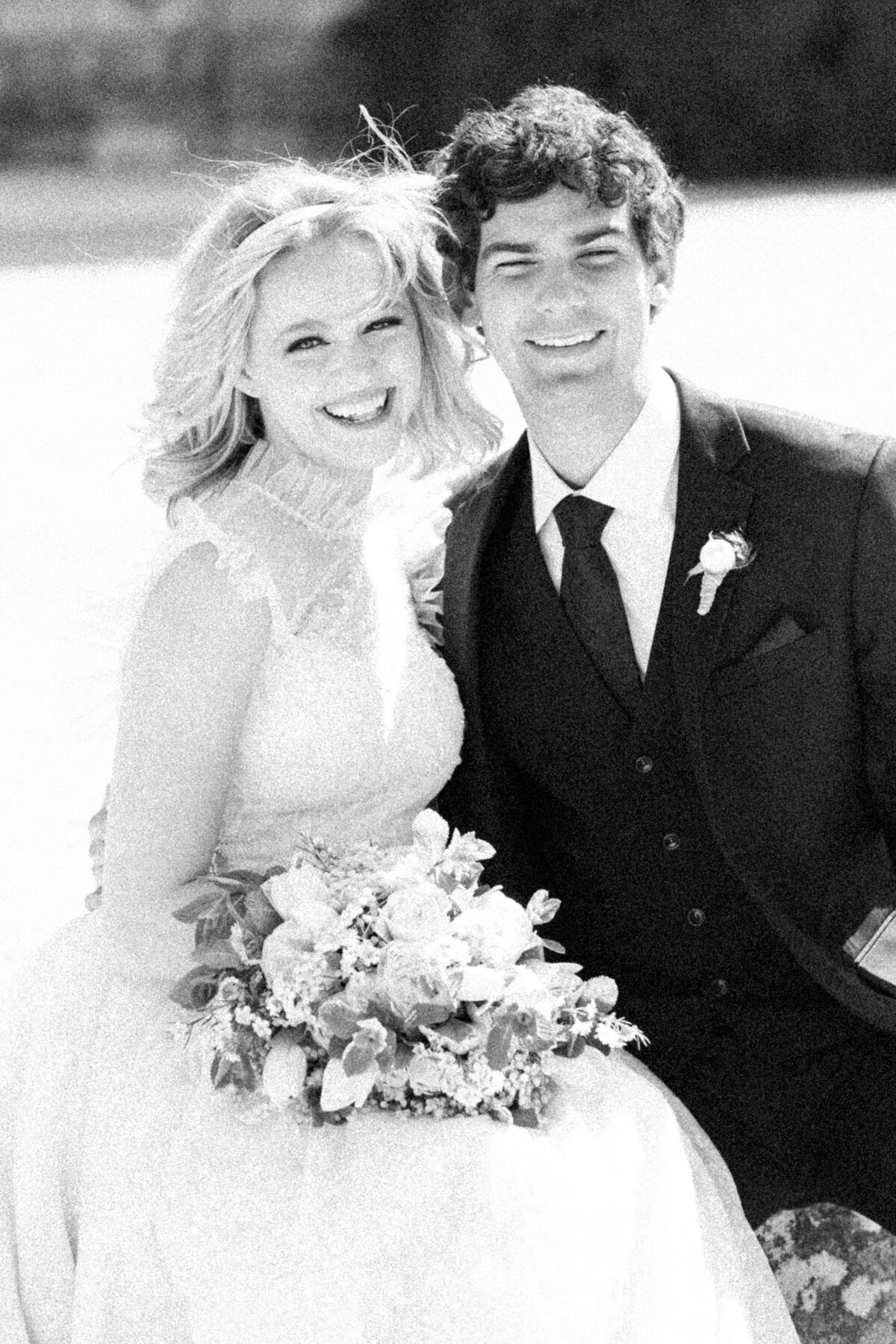 black and white image of a bride and groom sitting together and laughing