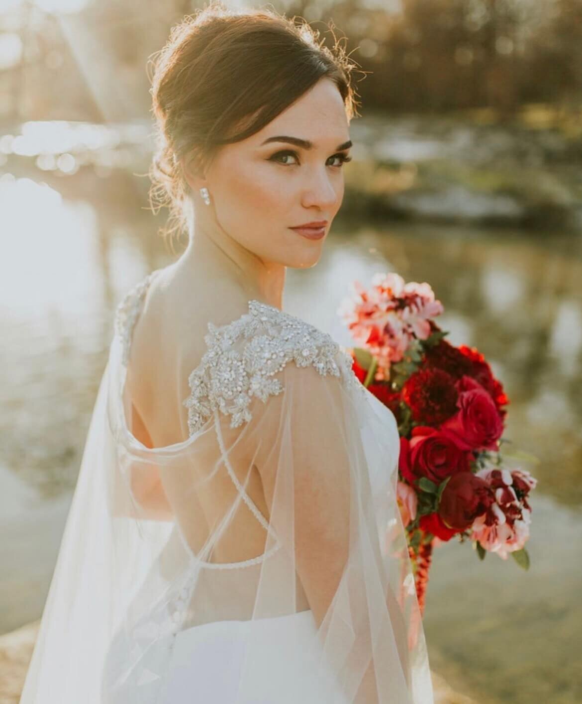 Modern bridal look featuring a sheer beaded cape detail and a bold red wedding bouquet. Styled by Mistique Makeup, offering mobile bridal hair and makeup in San Antonio and Austin. Book our wedding beauty team for flawless makeup and timeless elegance on your big day.