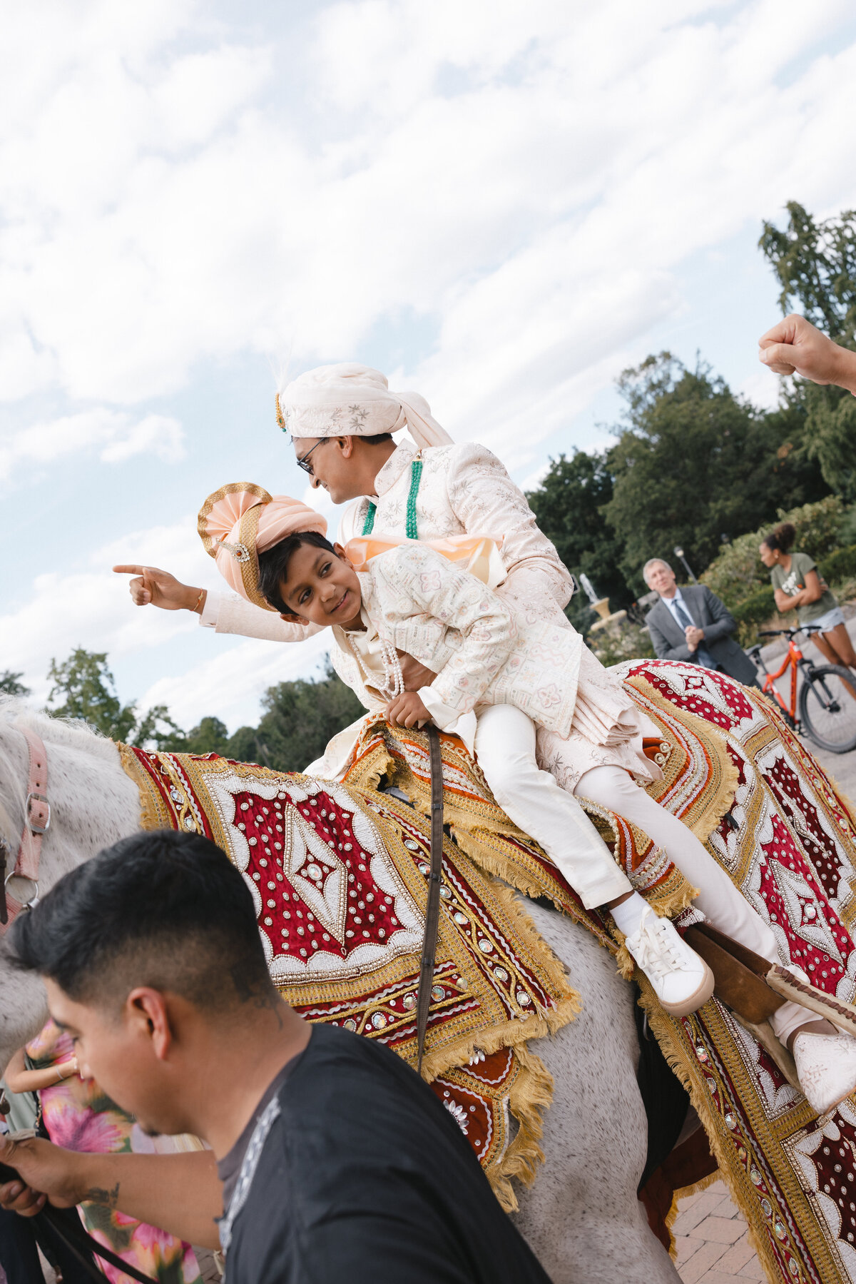 Baraat procession with groom and young family member riding a decorated horse during a South Asian wedding.