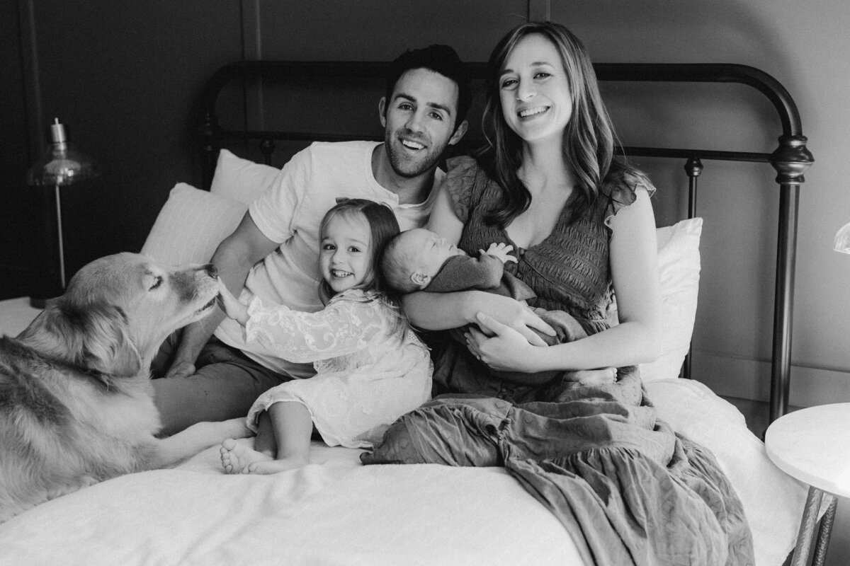 Mother and father on bed holding a baby with toddler and dog at Austin family photo session