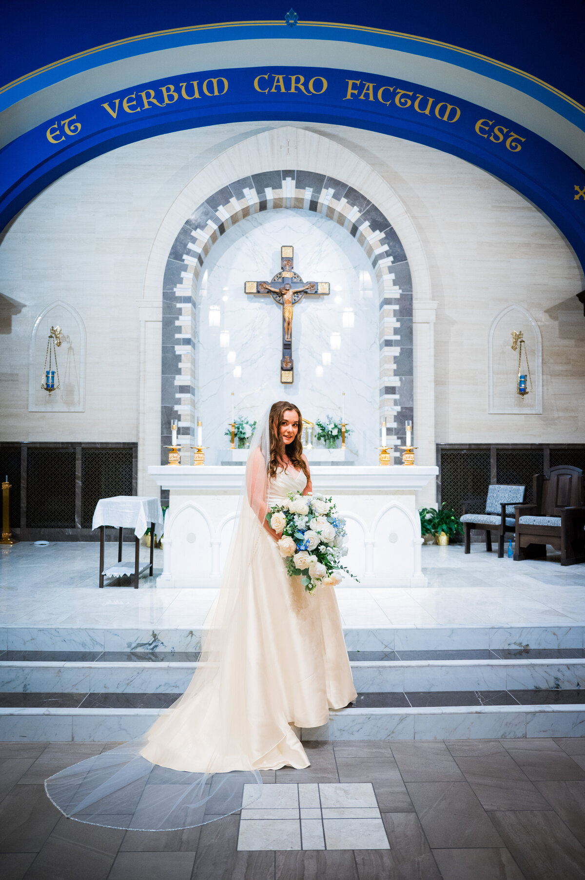 A bride gives the camera a soft smile as she stands on the altar of the church.