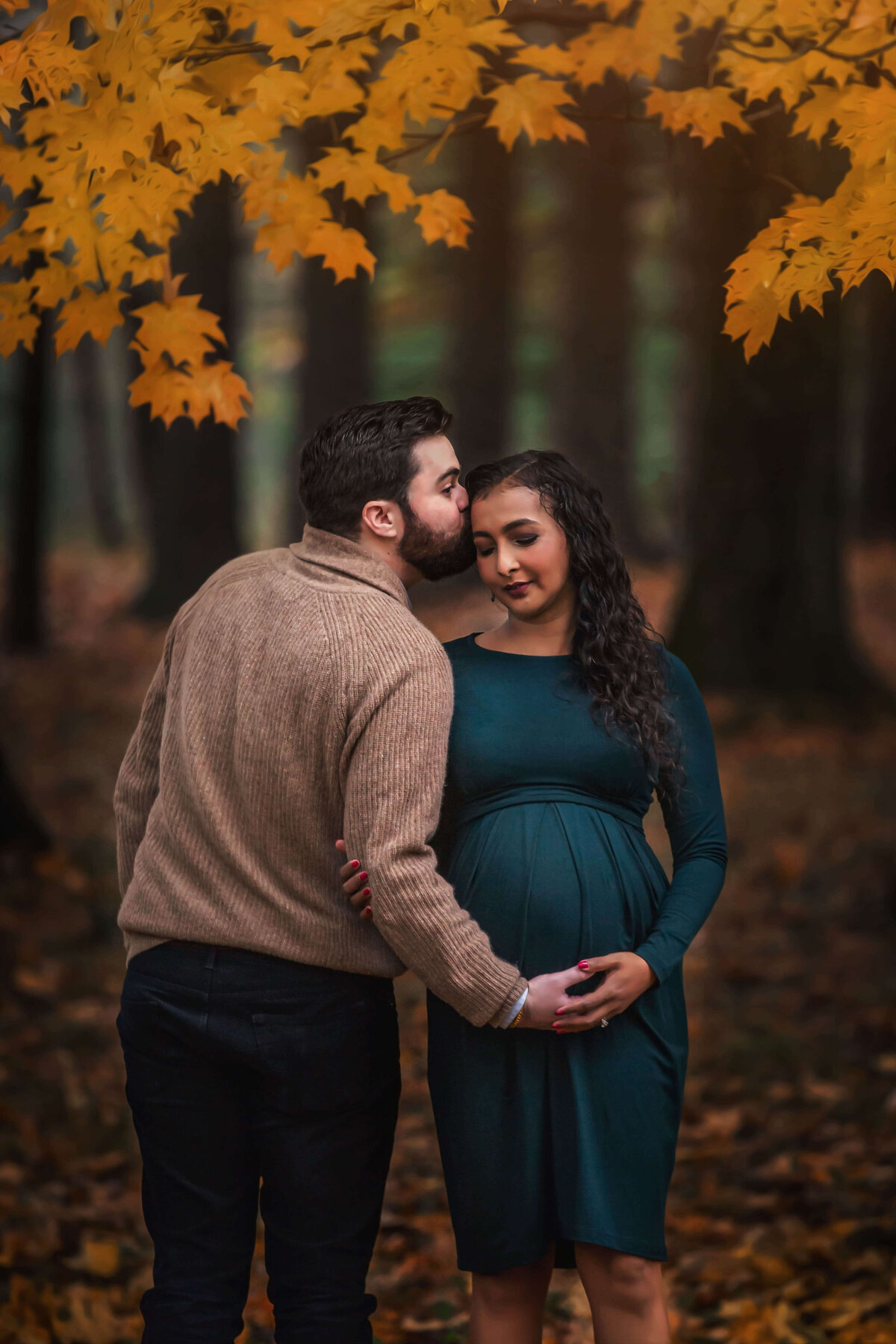 Expecting couple holding belly and standing in fall leaves
