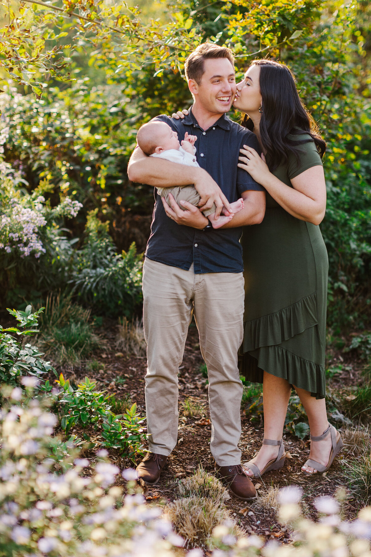 Woman kissing man on the cheek while he holds their newborn baby