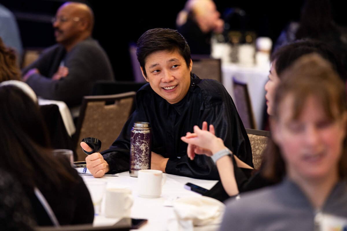 Ottawa event photos showing an asian man smiling at his table mates during a corporate conference.  Captured by JEMMAN Photography COMMERCIAL