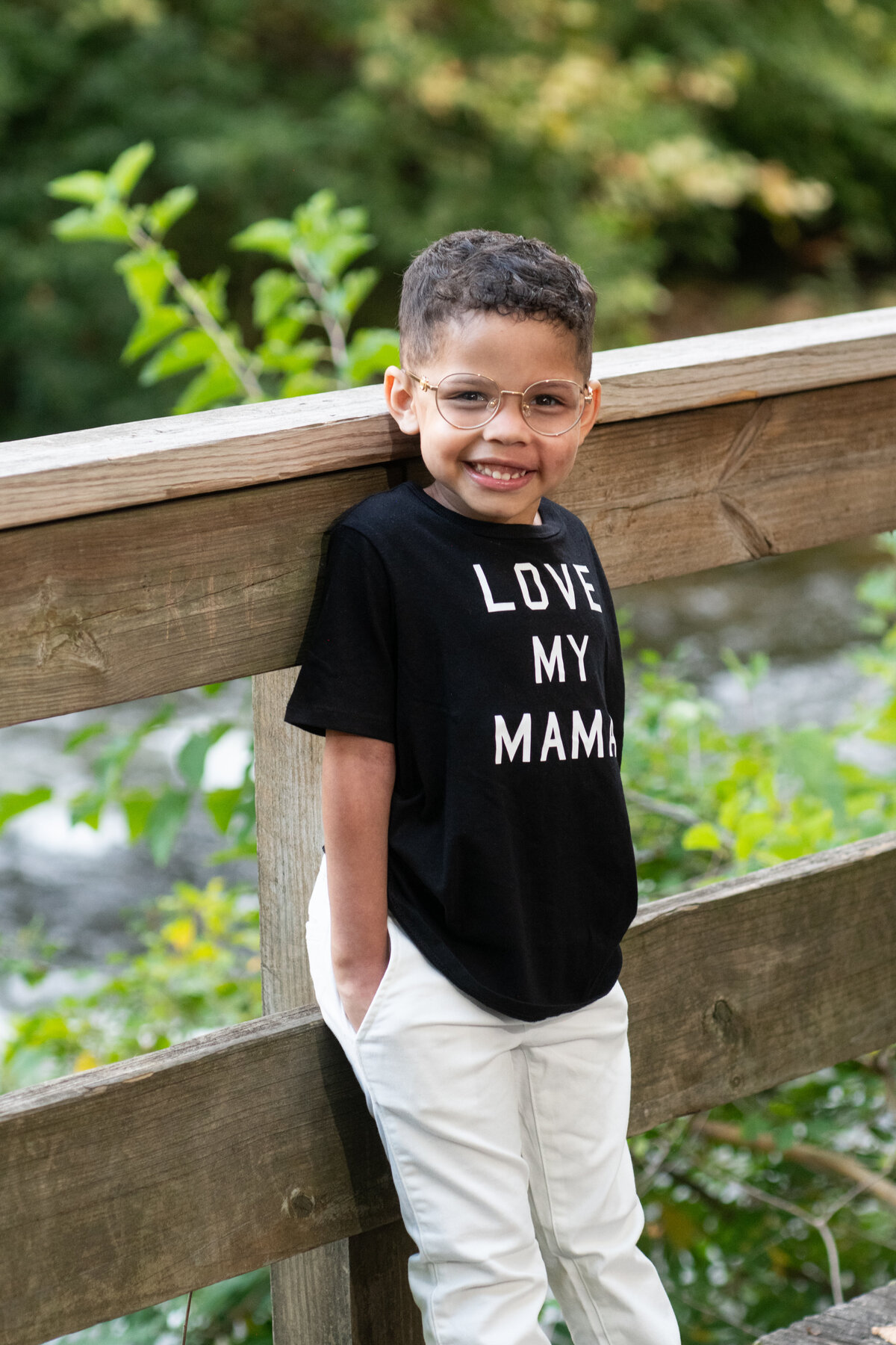 young boy smiles with hands in pockets on boardwalk near the river in Cuyahoga Falls