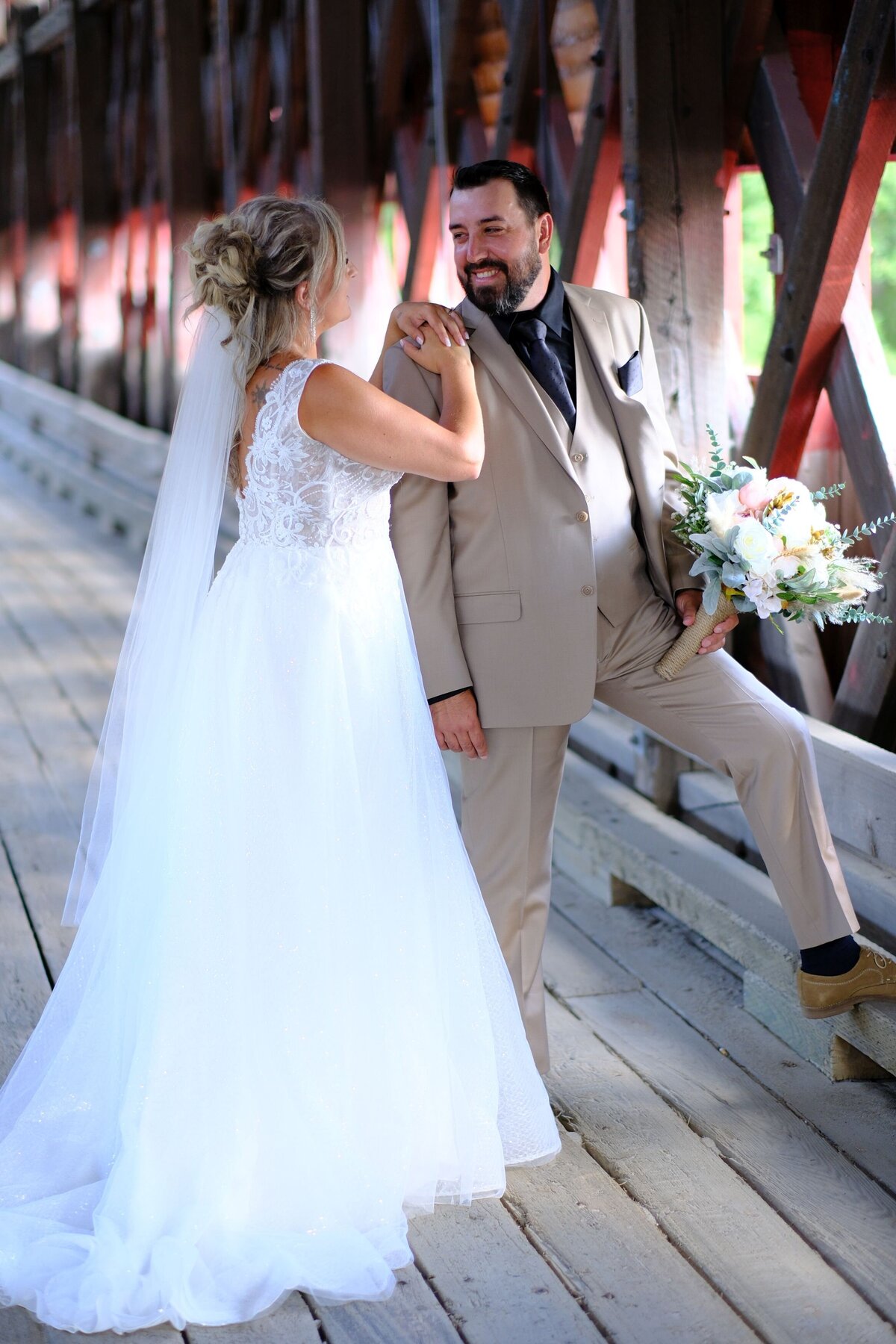 The bride and groom share a joyful moment, smiling at each other as the bride places her hand gently on the groom's shoulder. Their close proximity and expressions of happiness highlight their deep connection and love.