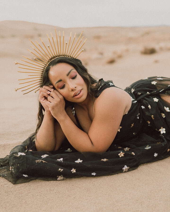 Woman wearing a star crown and black dress with stars laying on the sand dunes