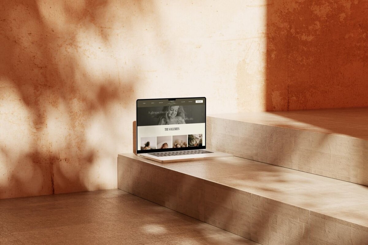 Laptop on warm terracotta stone steps displaying a photography gallery website in natural sunlight