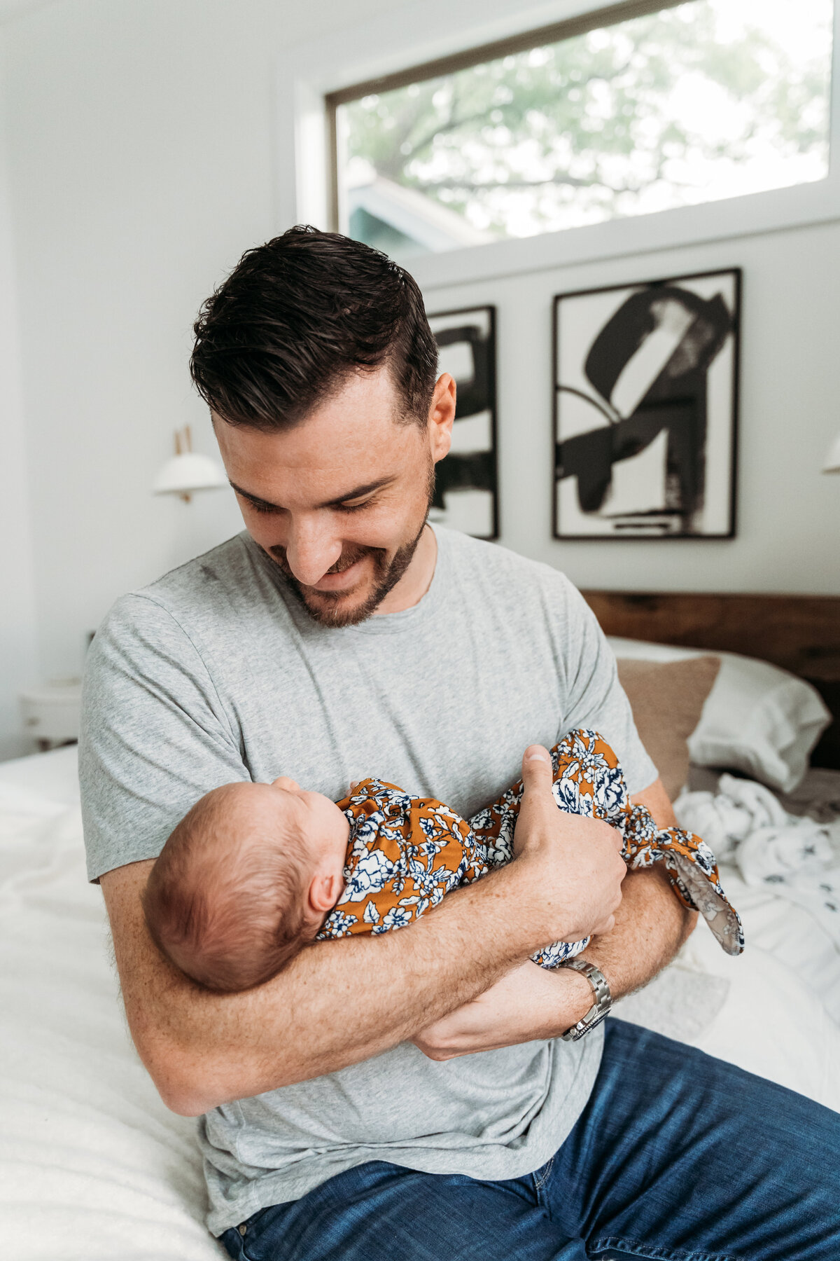 Newborn Photographer, a father holds his baby in his arms and smiles on his bed