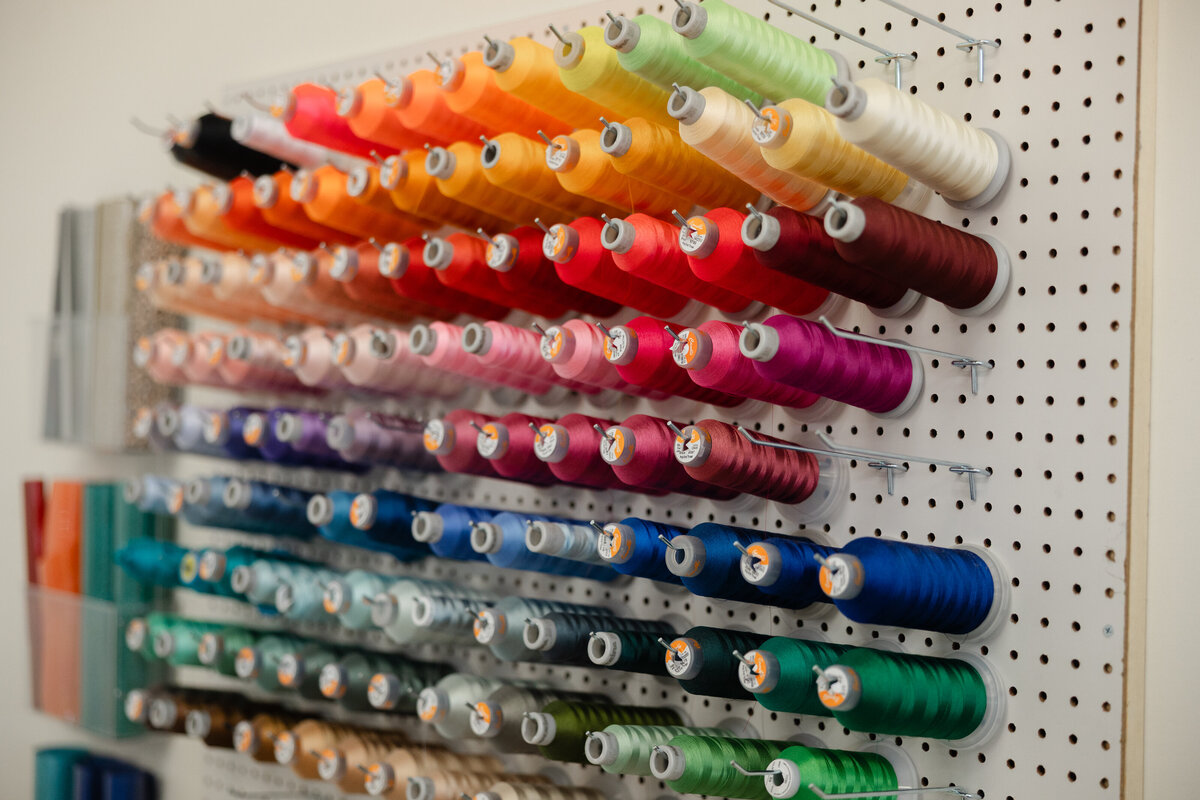 Rows of colorful embroidery threads displayed on shelves in studio. Photograph by Yucaipa branding photographer Kaitlyn Dawn Photography.
