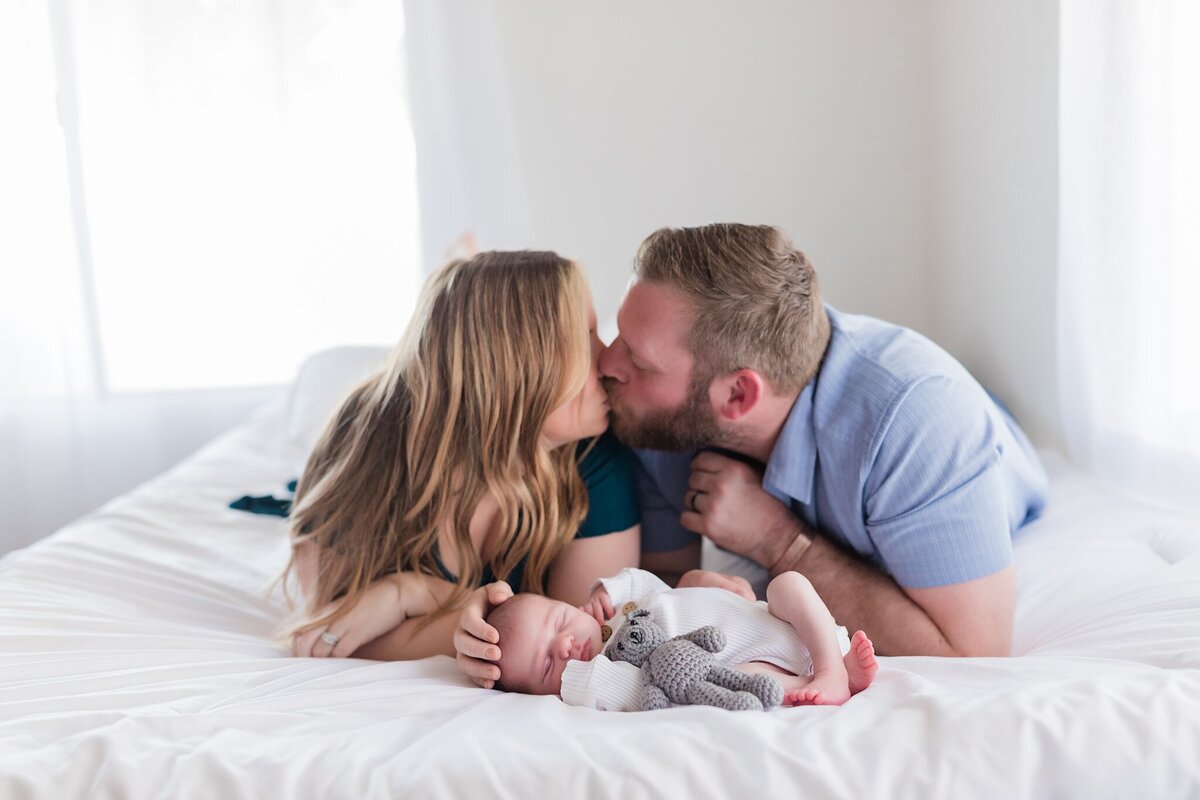 mom and dad kiss over newborn baby