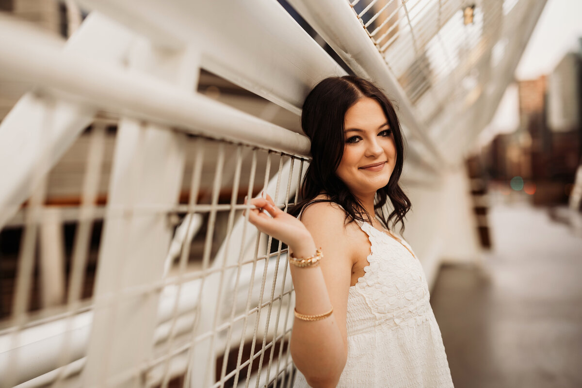 high school senior girl holds on to white metal gates in downtown Denver for senior photos