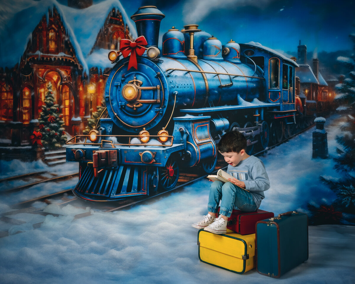 2 LITTLE GIRLS dressed in blue coats sitting on a wooden park bench infront of a large blue train