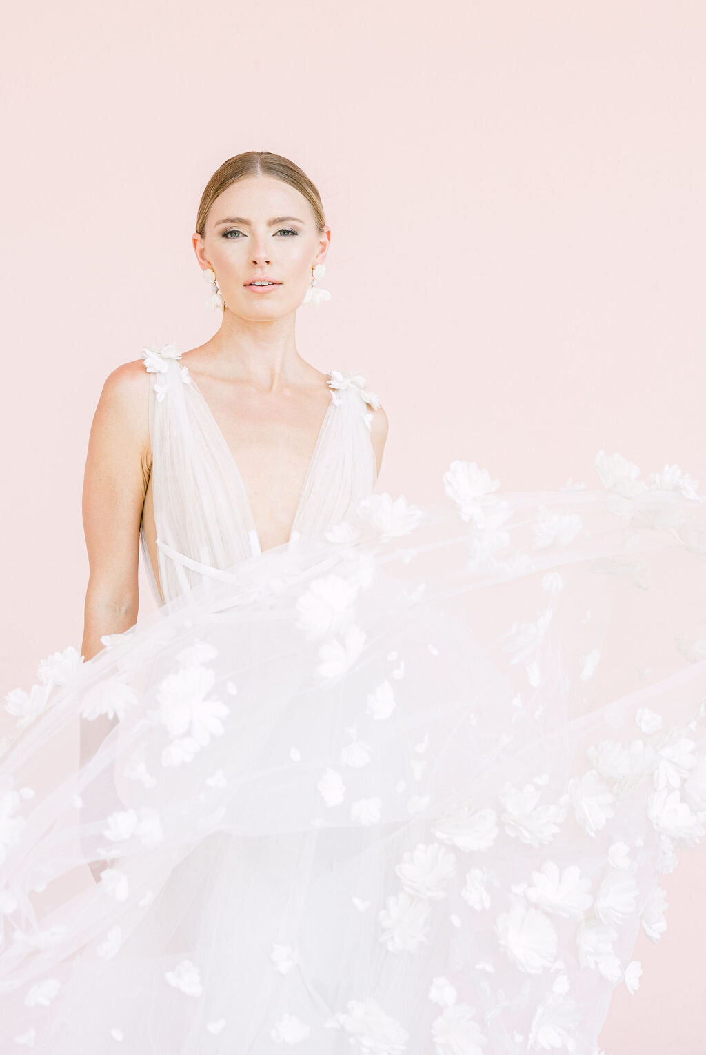 A stunning bride in a delicate floral wedding gown poses against a soft pink backdrop, capturing the essence of elegance and sophistication at a Sarasota, Florida wedding. Amia Marcell destination wedding photographer.