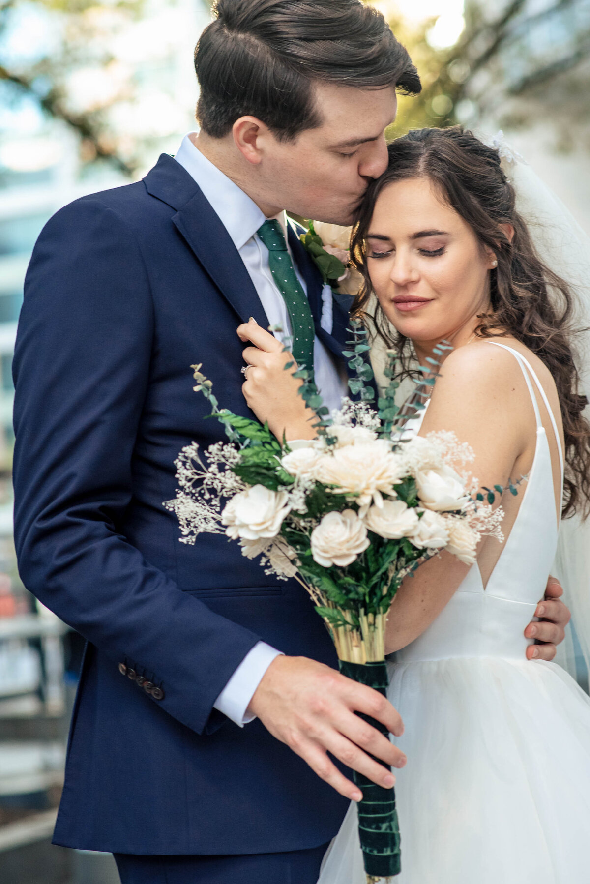 Up close portrait of a bride holding her groom's jacket lapel as he pulls her in and kisses her head by Charlotte wedding photographers DeLong Photography