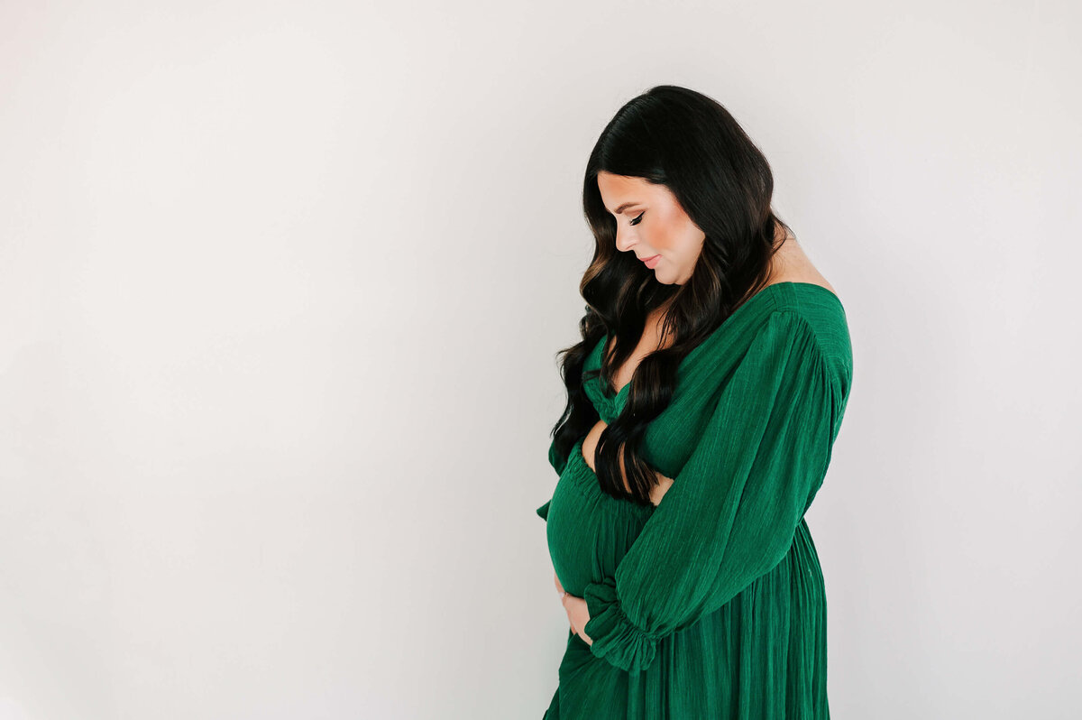pregnant mom in green dress looking down praying over baby bump in Springfield MO
