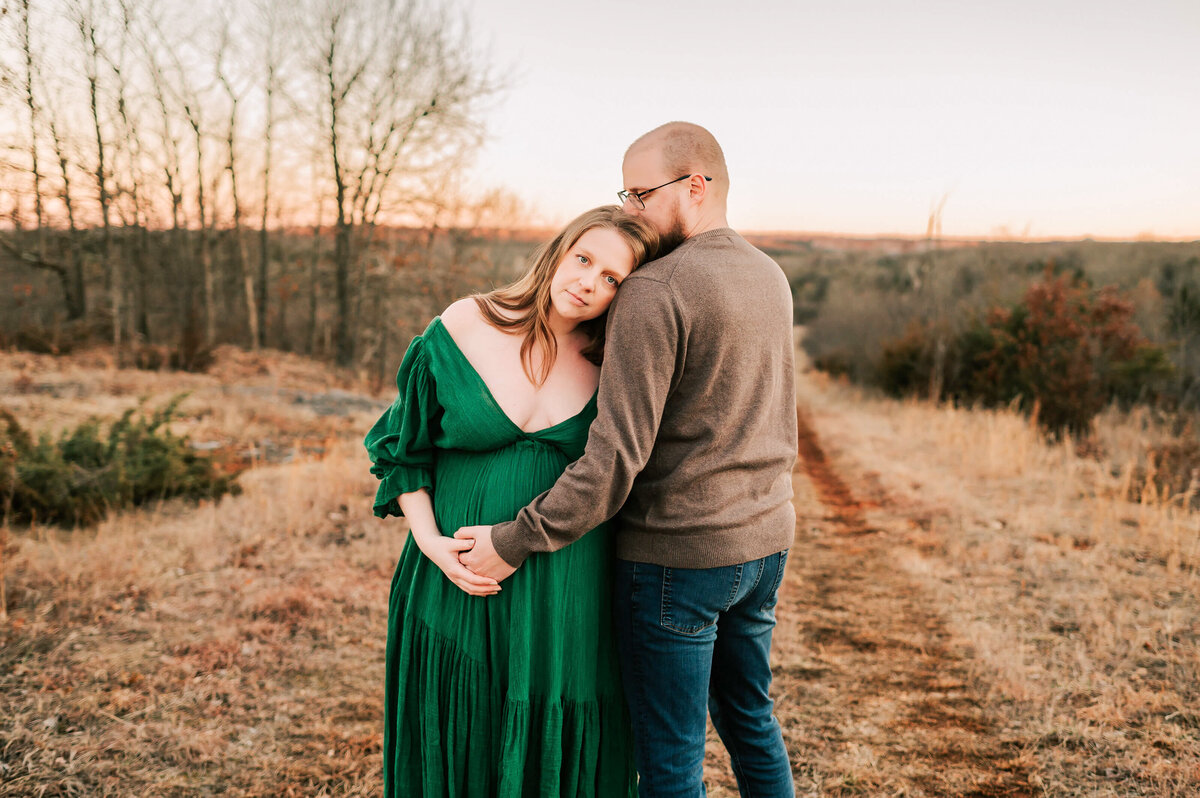 maternity pictures in Springfield MO of wife leaning on husbands shoulder both holding pregnant baby bump at sunset