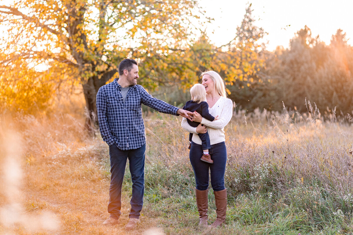 Dad reaching for moms hand smiling at mom while she is holding baby